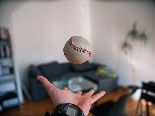 Selective closeup shot of a person tossing a gray baseball into the air - Фото, изображение