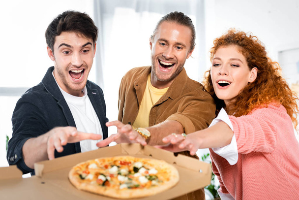 selective focus of three smiling friends taking pizza from box  - Photo, Image