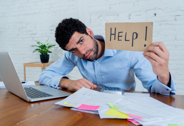 Young overwhelmed entrepreneur needing help paying off debts and bills in Small business financial problems. Worried desperate young man feeling stressed working through finances at home office. - 写真・画像