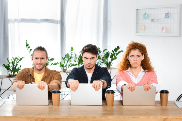 trois amis tristes assis à table et tenant des ordinateurs portables dans le bureau
  - Photo, image