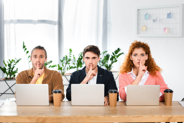 three friends sitting at table and showing shh gestures in office  - Photo, Image