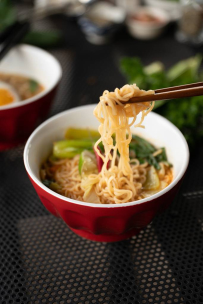 Vertical shot of chopsticks with noodles near the soup with a blurred background - Photo, image