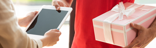 Panoramaaufnahme von Liefermann mit rosa Geschenk und der Übergabe eines digitalen Tablets an Frau  - Foto, Bild