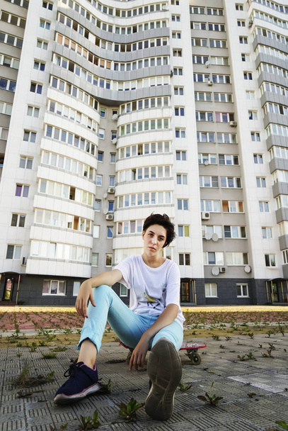 European pretty beautiful young woman in blue jeans in sneakers sitting  on the ground on the street in the city on modern building background - Фото, зображення