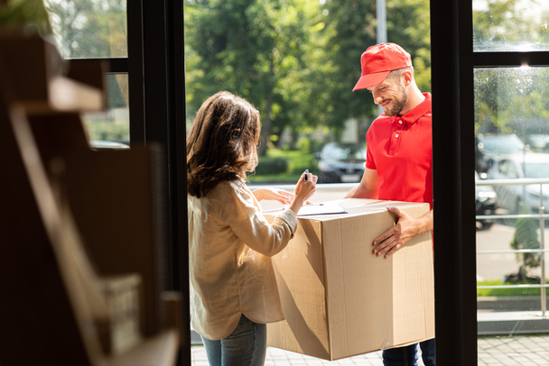 selective focus of happy delivery man holding box near woman with pen  - Foto, afbeelding