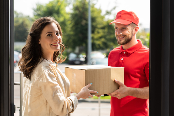 cheerful woman smiling near happy delivery man with box  - Zdjęcie, obraz