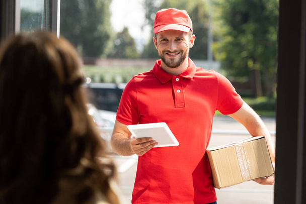 selective focus of cheerful delivery man holding digital tablet and box near woman  - Foto, imagen