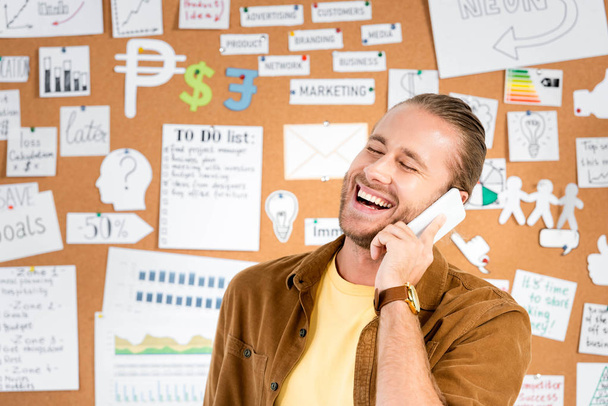 handsome and smiling businessman talking on smartphone in office   - Foto, Imagen