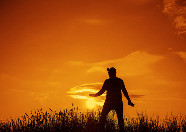 silhouet van een jonge man met behulp van mobiele telefoon bij zonsondergang. Vakantie-en technologie concept. Silhouet van de man hand houden zon op de zomer ochtend Sunrise  - Foto, afbeelding