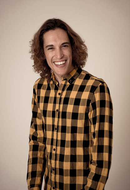 Studio portrait of young teenager man with brown long hair wearing checked shirt feeling confident and relaxed posing and modeling. Isolated on neutral background. In lifestyle and youth culture. - Foto, Imagem