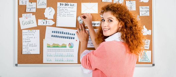 panoramic shot of attractive businesswoman in pink sweater putting card on wooden board   - Foto, Imagem