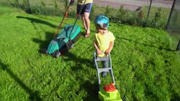 Happy active toddler boy with toy lawn mower in front of father. Gimbal movement - Footage, Video