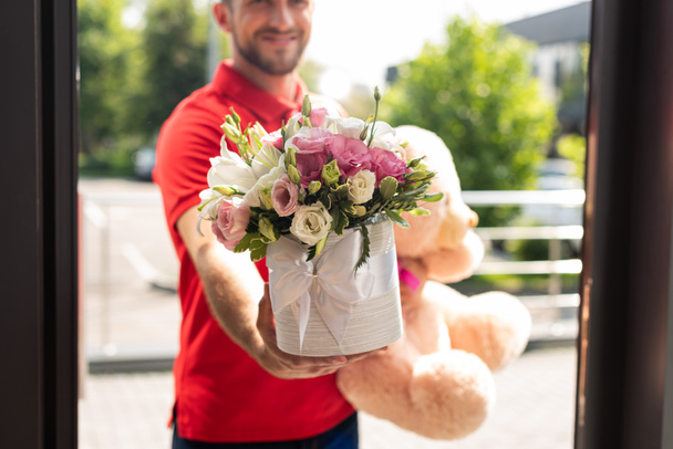 vista ritagliata di barbuto consegna uomo in possesso di orsacchiotto e fiori
  - Foto, immagini
