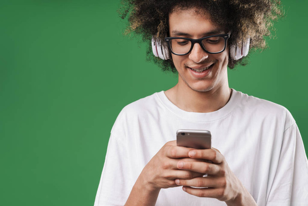 Photo closeup of handsome man with afro hairstyle smiling while using cellphone and headphones - Foto, Bild