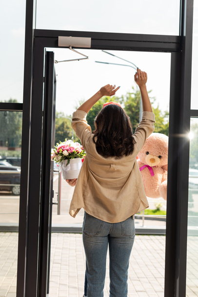 back view of woman standing with hands above head near delivery man with gifts  - Photo, Image