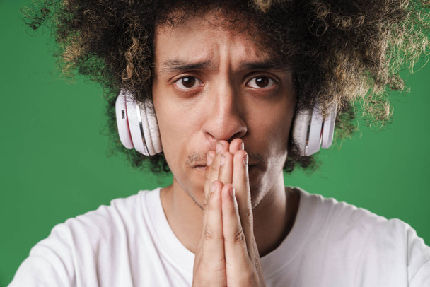 Guy posing isolated over green wall background listening music with headphones make hopeful please gesture. - Valokuva, kuva