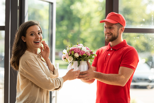 bearded and happy delivery man giving flowers to beautiful woman  - Valokuva, kuva