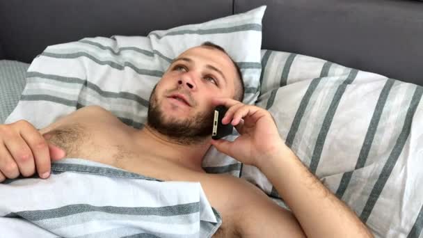 Un hombre joven está acostado en la cama y hablar o llamar a un teléfono inteligente, vista superior
 - Metraje, vídeo