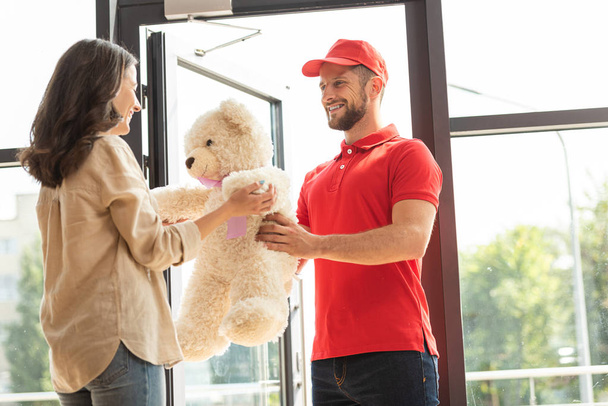 happy girl receiving teddy bear from bearded man in cap  - 写真・画像
