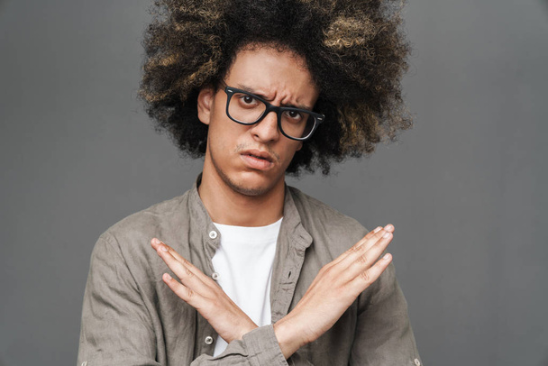 Sad displeased teenage guy posing isolated over grey wall background showing stop gesture. - 写真・画像