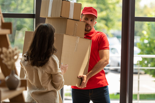 foco seletivo de homem de entrega bonito segurando caixas de papelão perto da mulher em casa
  - Foto, Imagem