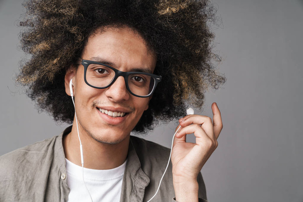 Photo closeup of young happy man with afro hairstyle smiling at camera and using earphones - Foto, afbeelding