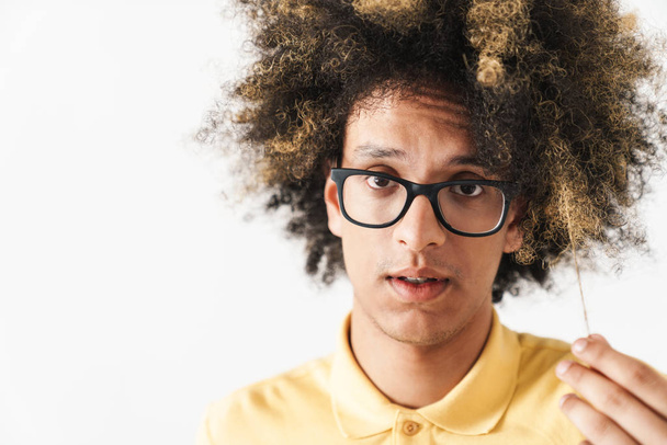 Confused young curly man isolated over white background looking camera holding hair. - Foto, immagini