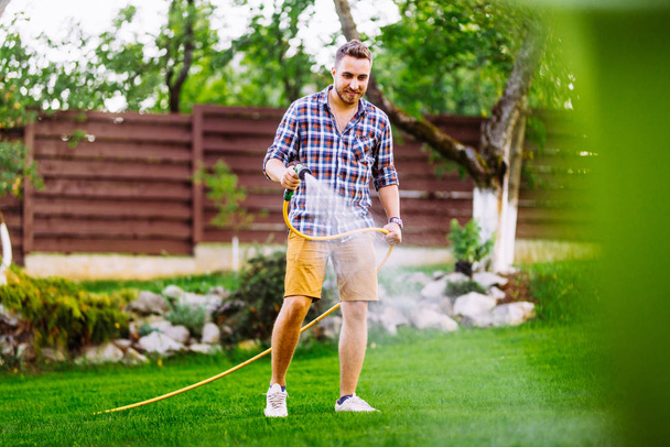 Caucasian man working on grass irrigation. Hose manual system, watering the lawn - 写真・画像