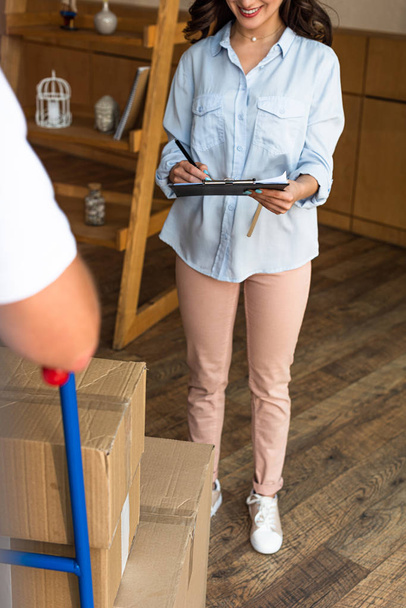cropped view of happy woman signing paper while holding clipboard near delivery man  - Foto, imagen