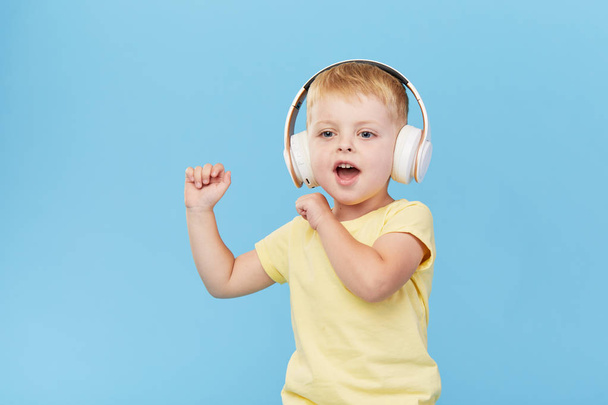 Happy smiling child enjoys listens to music in headphones over colorful blue background. Vivid and fun emotions, happy child with pleasure listens to songs in wireless headphones - Foto, immagini