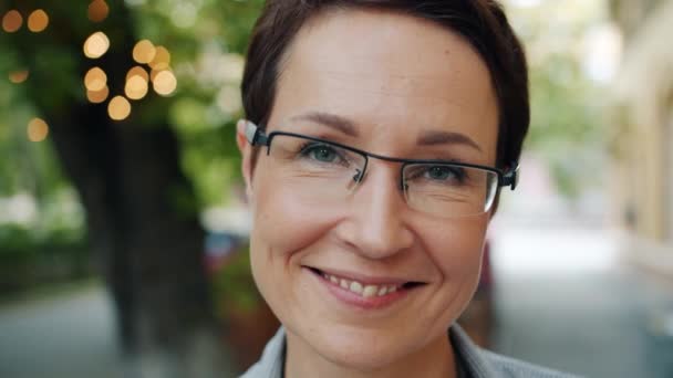 Close-up portrait of mature businesswoman in glasses smiling at camera outdoors - Filmagem, Vídeo