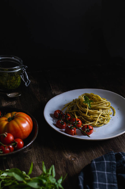 Spaghetti pasta met basilicumpesto en tomaten, houten tafel - Foto, afbeelding