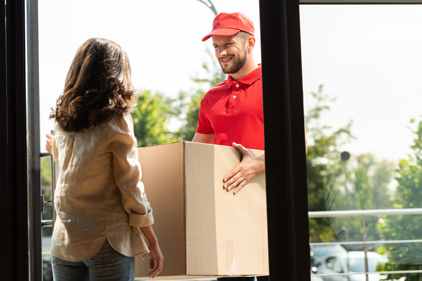χαρούμενα delivery man in cap holding box κοντά γυναίκα  - Φωτογραφία, εικόνα