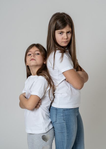 Portrait of two young siblings standing back to back not talking to each other after having an argument. Sisters not interacting angry and mad one to another in bad relationship. Studio shot. - Φωτογραφία, εικόνα