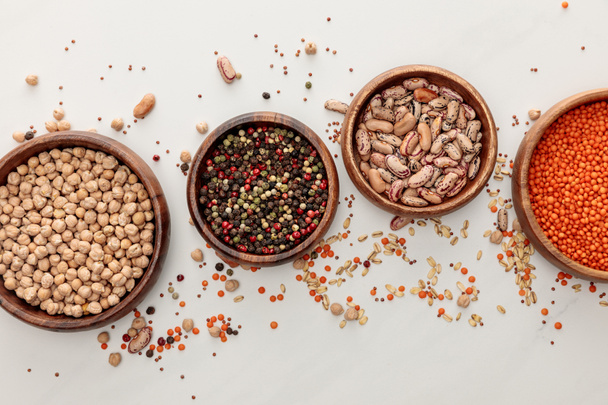 top view of wooden plates with chickpea, lentil, peppercorns, and beans near scattered grains on marble surface - Photo, Image