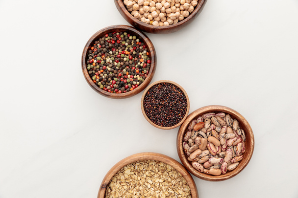 top view of wooden bowls with black quinoa, oatmeal, beans, peppercorns and chickpea on white marble surface - Photo, Image