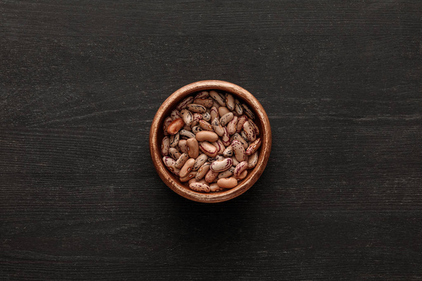 top view of brown bowl with raw beans on dark wooden surface with copy space - Photo, Image