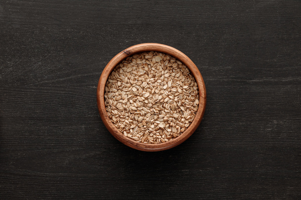 top view of brown bowl with raw oatmeal on dark wooden surface with copy space - Foto, Bild