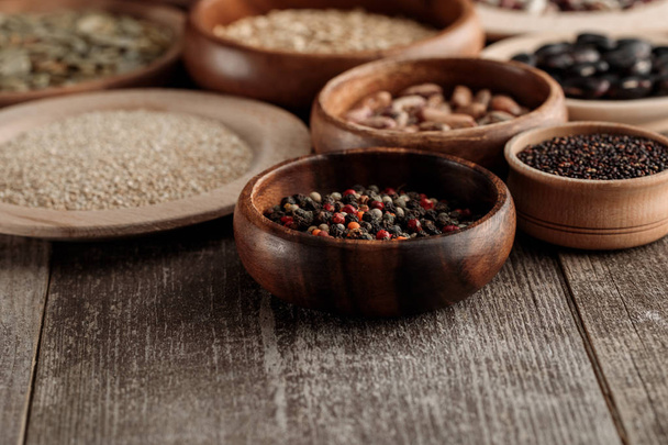 wooden bowls and plates with peppercorns, grains and beans on brown table - Photo, Image