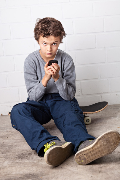 Cool Boy sitting on his skateboard, holding a smartphone - Фото, изображение