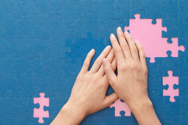 cropped view of woman covering blue jigsaw puzzle on pink background - Photo, Image