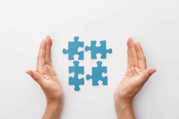 vista ritagliata delle mani della donna vicino a pezzi di puzzle blu su sfondo bianco
 - Foto, immagini