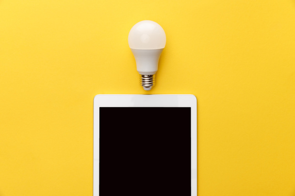 top view of light bulb and digital tablet with blank screen on yellow background - Photo, Image