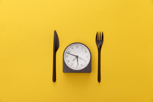 top view of clock between knife and fork on yellow background - Photo, Image