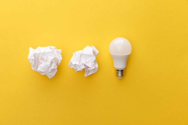 top view of crumpled paper near light bulb on yellow background - Photo, Image
