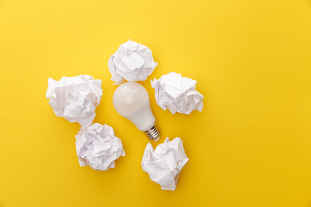 top view of light bulb between crumpled paper on yellow background - Foto, Imagem