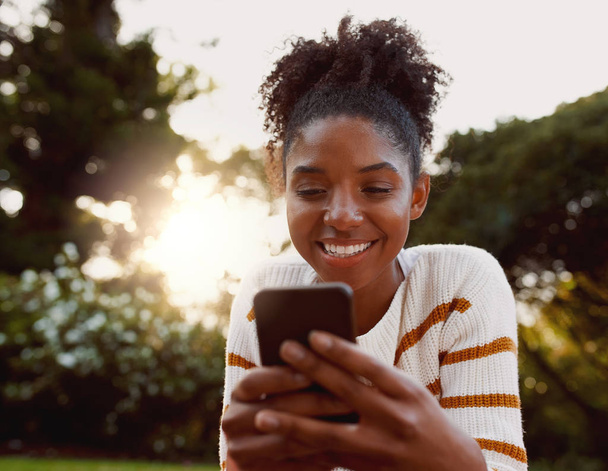 晴れた日に公園で携帯電話を使用してアフリカ系アメリカ人の若い女性の肖像画 - 携帯電話で非常に幸せな女性 - 写真・画像
