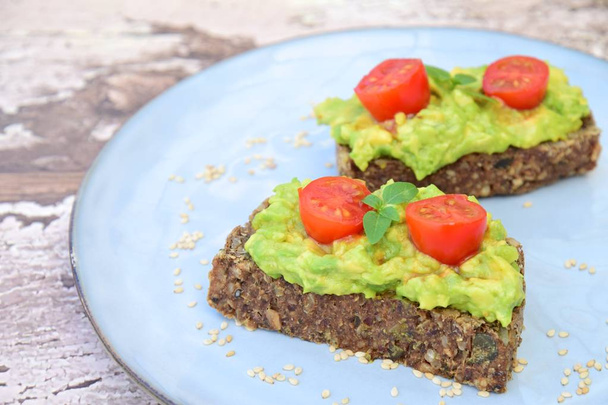 Slices of gluten free pumpkin seed buckwheat bread with mashed avocado, cherry tomato and basil leaves - Photo, Image
