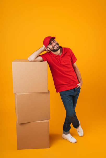 Portrait of cheerful delivery man in red uniform smiling while s - Photo, image