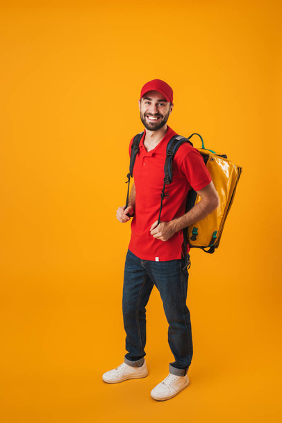 Image of joyful delivery man in red uniform carrying backpack wi - Фото, изображение